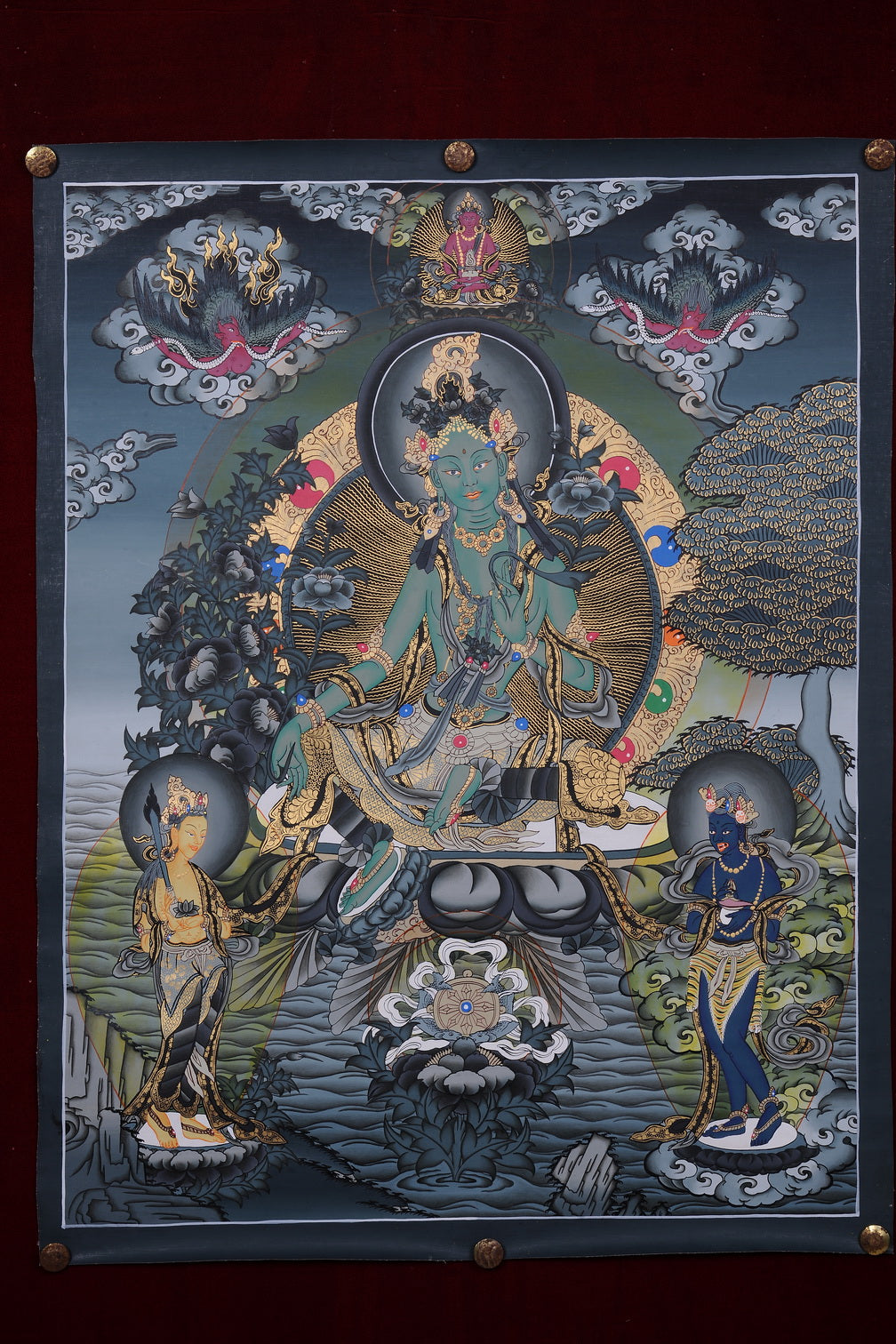 Hand-painted thangka of Green Tara on a lotus seat holding blue utpala flowers, with a Buddha above and two attendants below