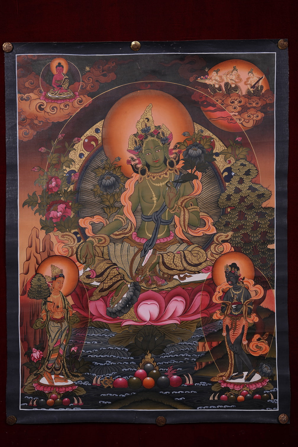 Hand-painted thangka of Green Tara seated on a pink lotus with her right leg extended, a Buddha above and attendant figures below