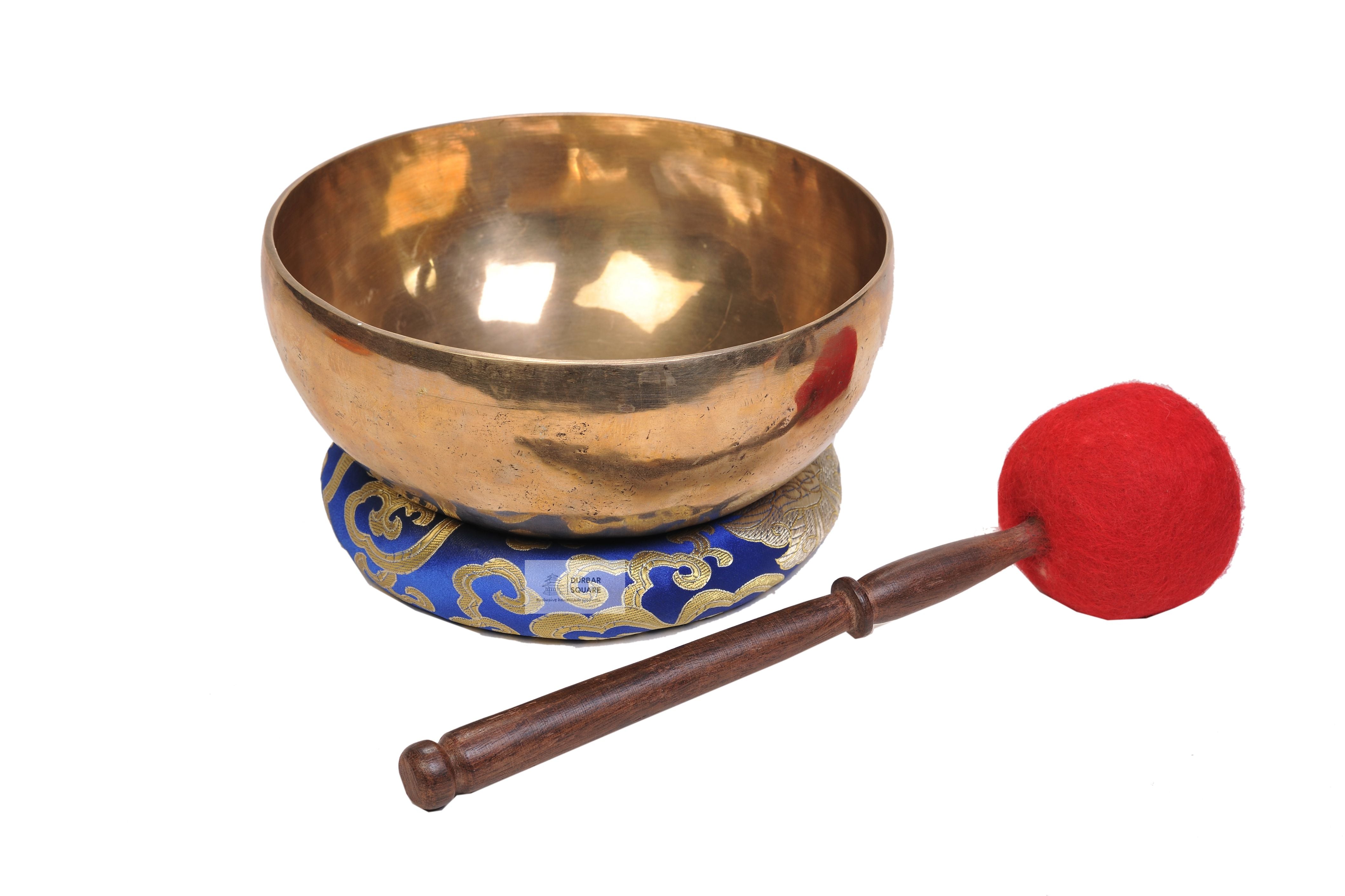 Plain polished brass singing bowl on a blue brocade cushion with a red felt mallet