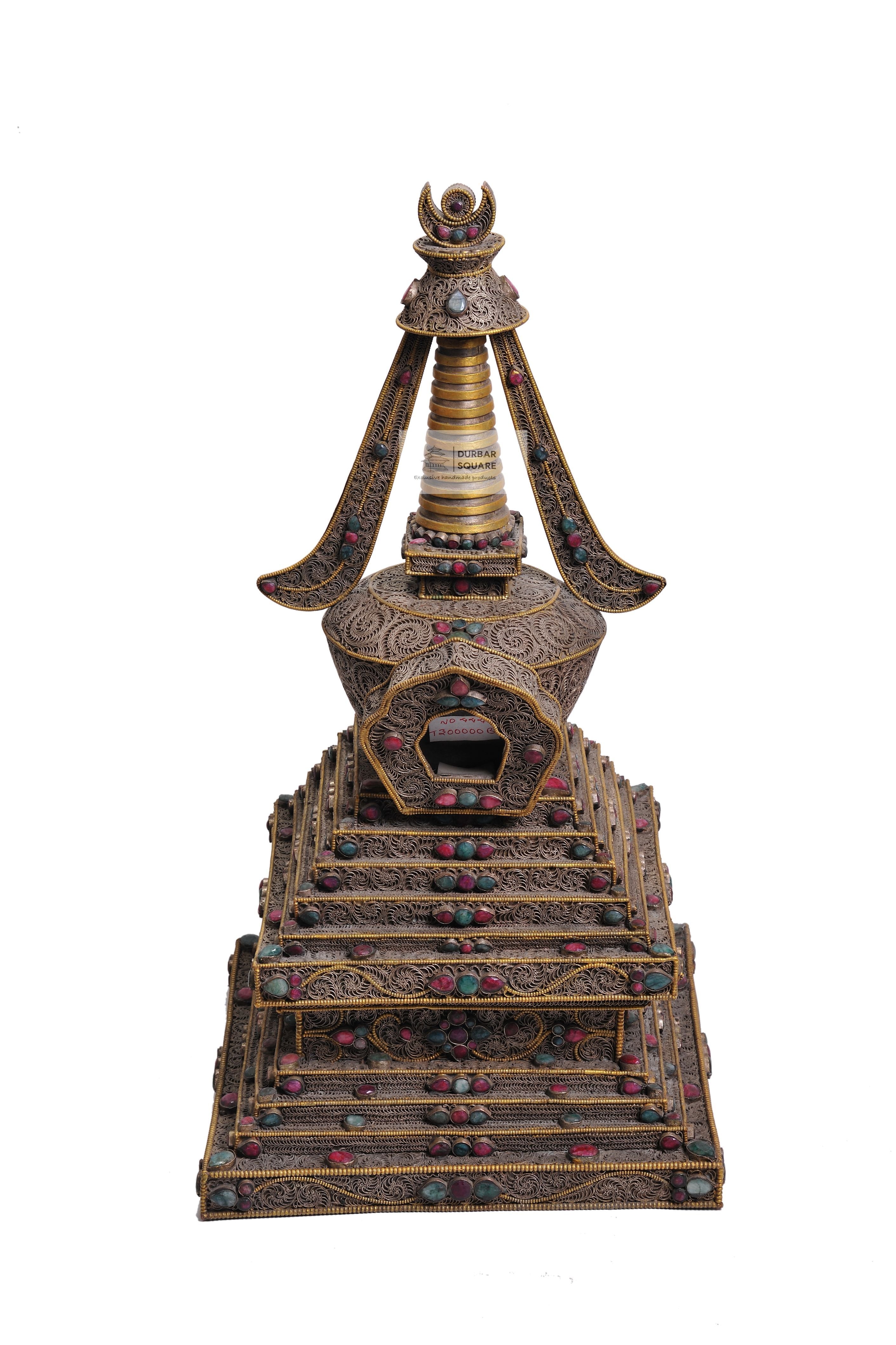 Ornate filigree copper stupa inlaid with coloured stones on a stepped plinth, with hanging banners from the spire