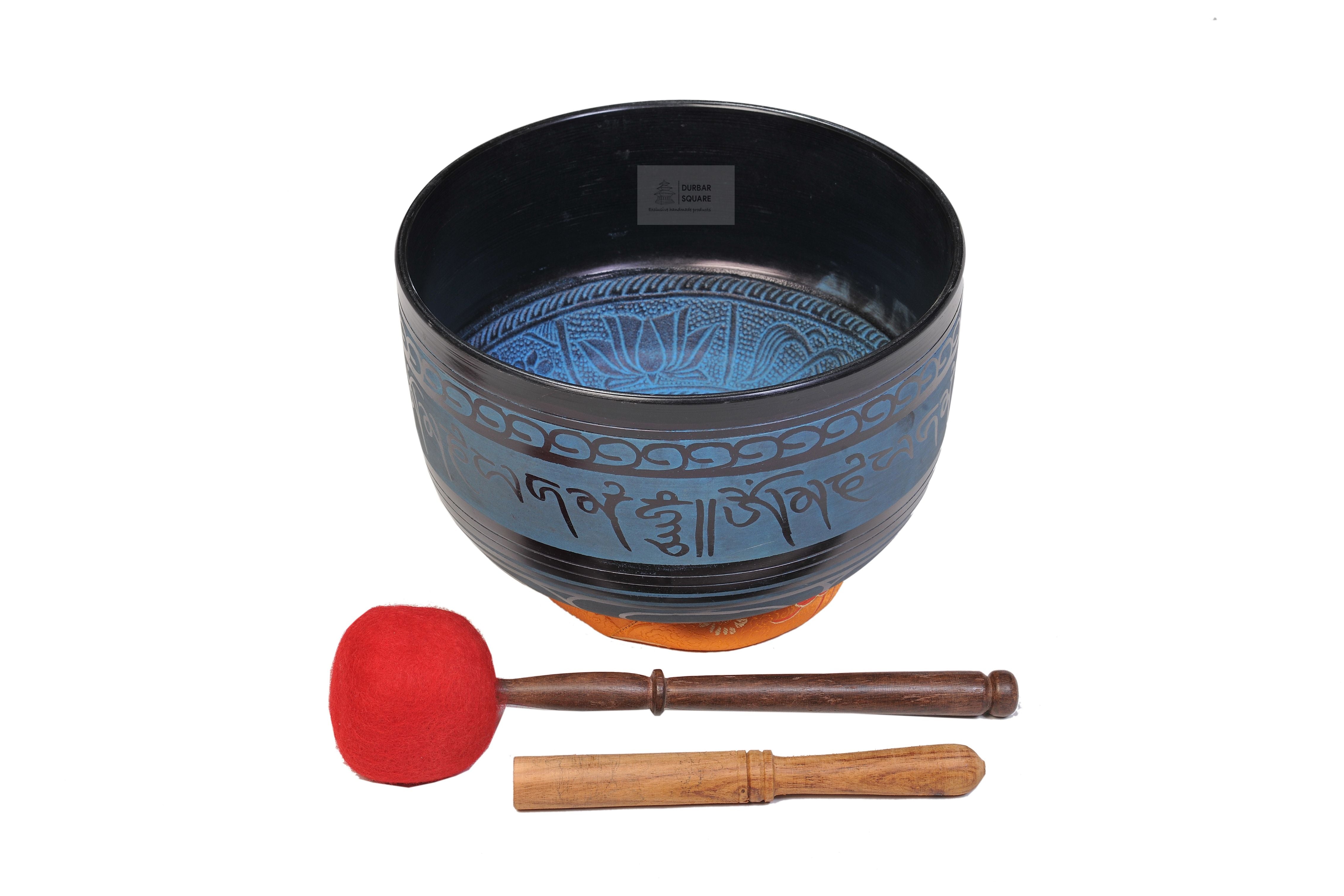 Dark carved singing bowl with mantra lettering around the body and a lotus design inside, with two strikers