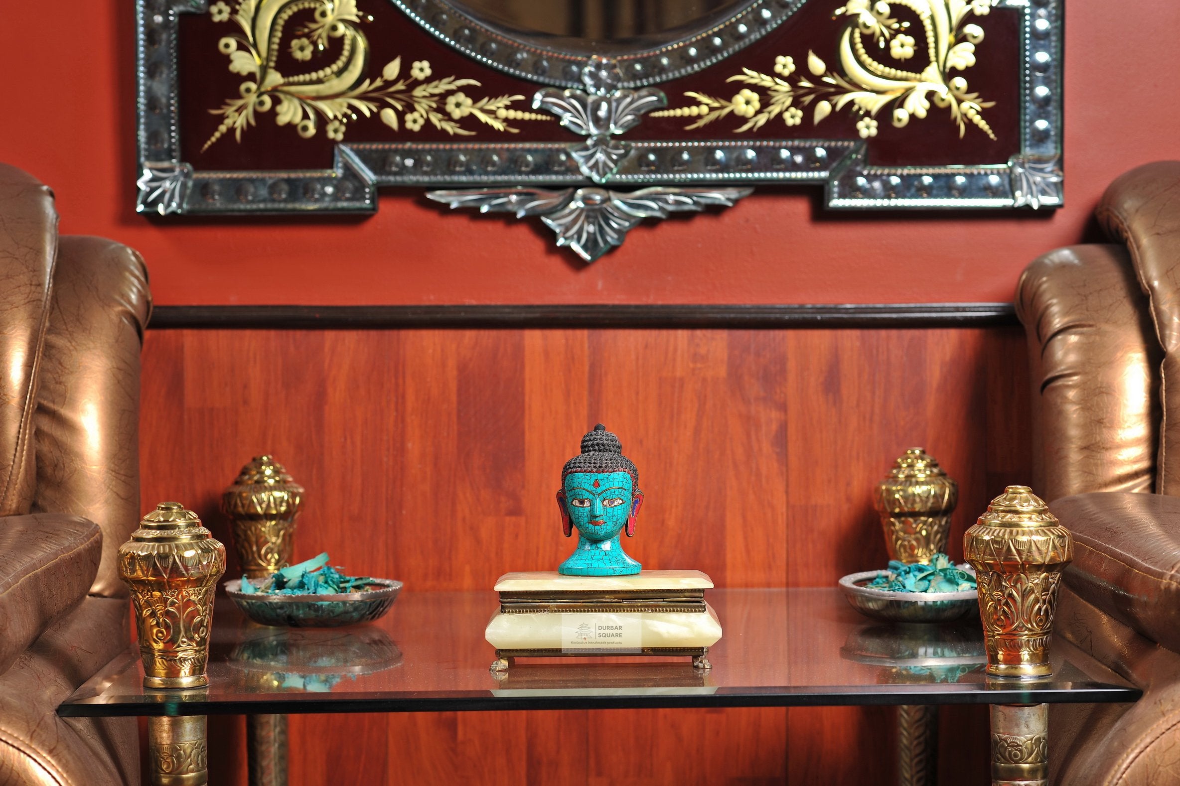 Small turquoise-finished Buddha head statue with tight curls and elongated earlobes on a cream stand