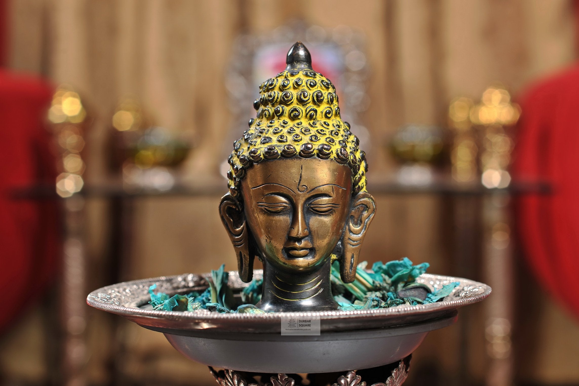 Bronze Buddha head statue with golden curls, elongated earlobes and closed eyes
